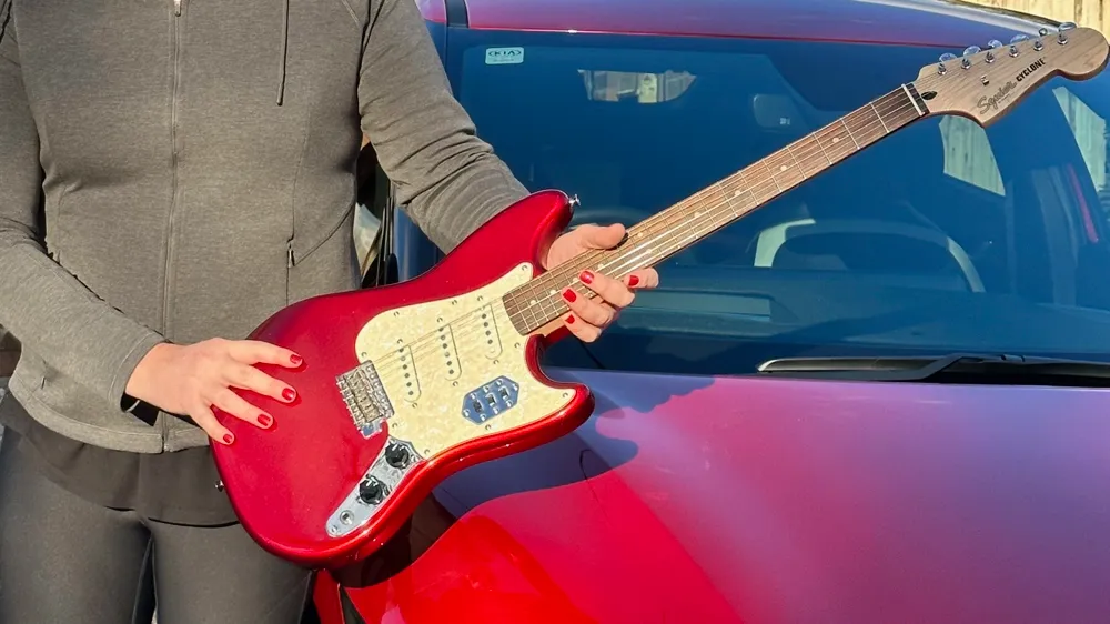 Squier Cyclone in Candy Apple Red set against a red Kia EV6 car